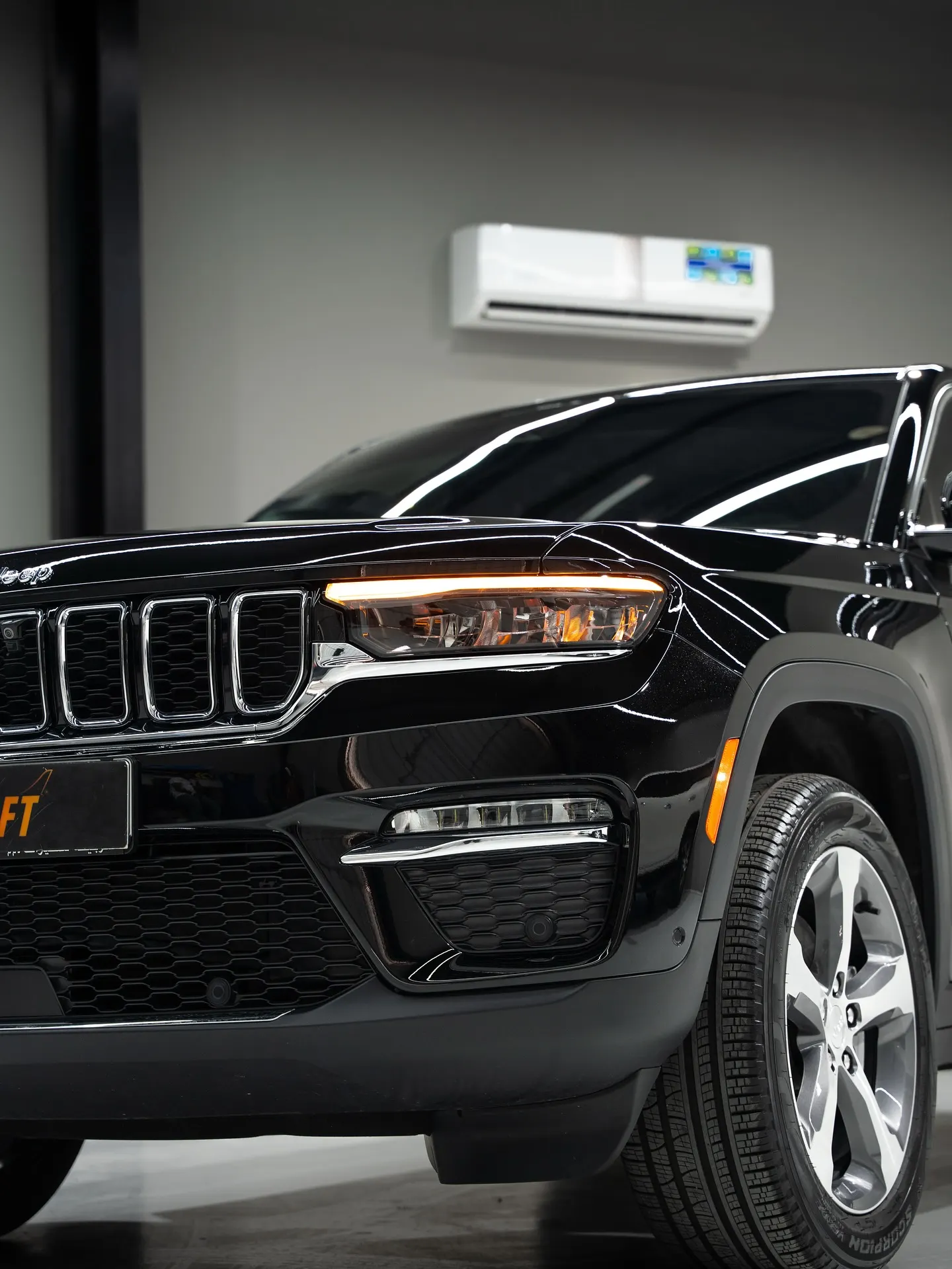Front three-quarter detail of a black SUV under showroom lighting, the grille, headlamp and wheel catching the reflection