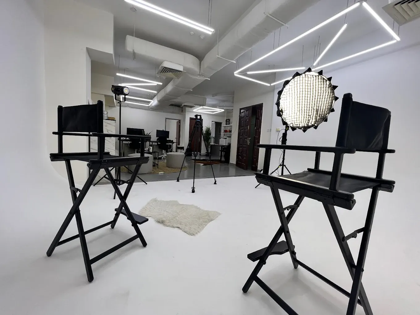 Wide view of a studio interior with LED strip lighting, director's chairs and a beauty dish